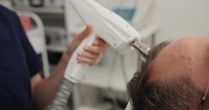 Female clinician performing handheld hair treatment device on male patient scalp for clinic therapy.