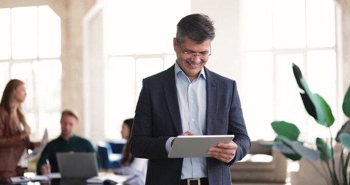 Smiling middle aged businessman ceo managing digital workflow on tablet device analyzing sales success monitoring project updates enjoying work productivity during active corporate workday in office