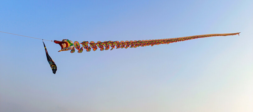 Colorful Dragon-Shaped Kite with Long Decorative Tail Flying Against Blue Sky. 