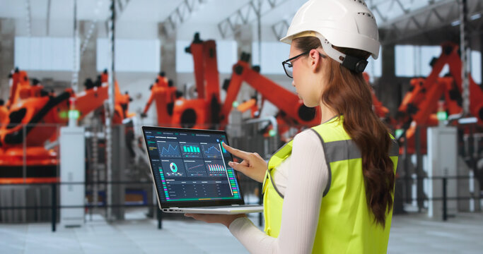 Young Female Engineer Monitors Factory Systems Using Laptop
