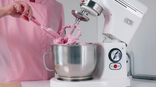 Scraping pink macaron mixture from a whisk with a silicone spatula