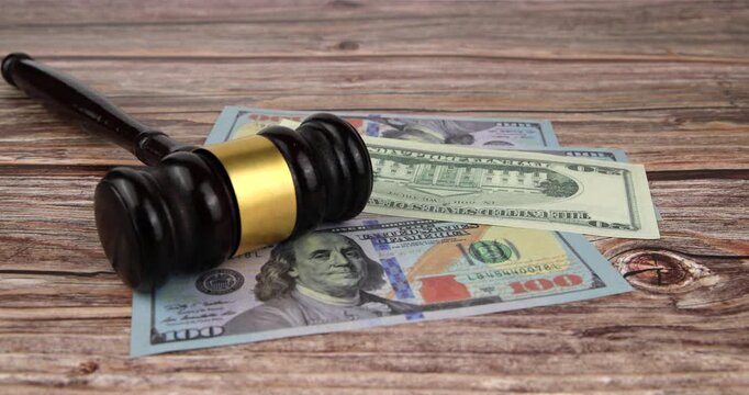 Wooden judge gavel on table with US dollar banknotes falling around in horizontal orientation representing financial crime and legal corruption