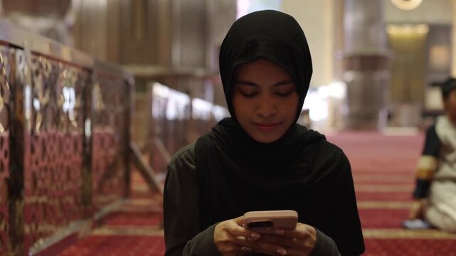 Muslim woman in hijab using smartphone inside mosque