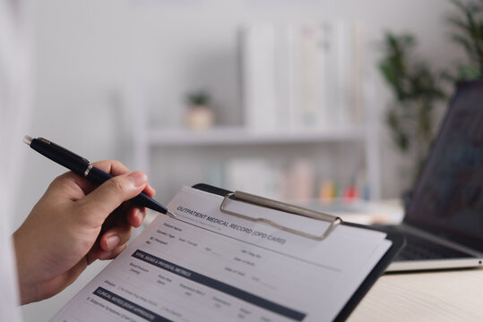 Outpatient medical record form on clipboard reviewed with pen beside laptop for clinical documentation healthcare administration and record management