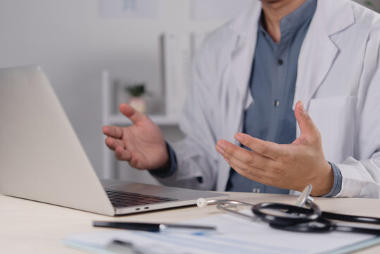 Healthcare professional gesturing beside laptop with stethoscope on desk for digital medical communication in modern office workspace