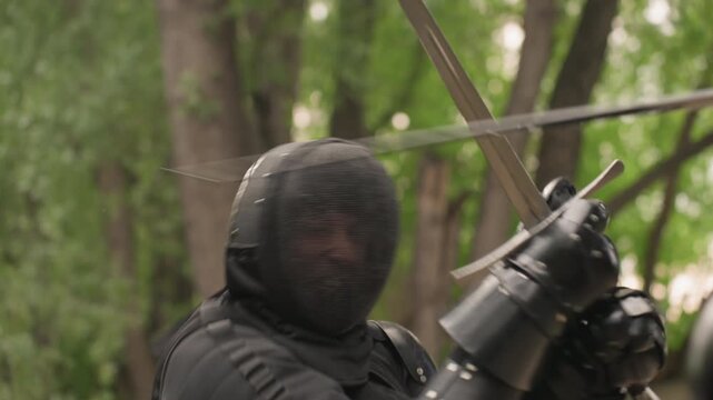 Close up of person in black fencing gear actively engaging with another fencer demonstrating sword techniques and movements. scene features protective equipment including mesh helmet padded