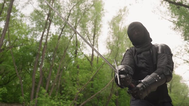 Close up of person in black medieval armor demonstrating sword fighting techniques with two swords by moving them through various positions. subject holds and manipulates weapons