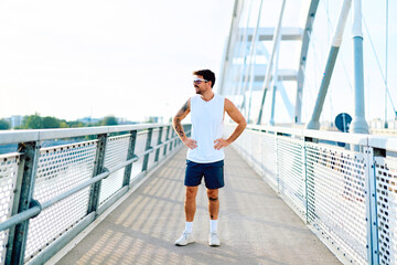 Naklejka premium Male runner taking a break on a modern bridge during a workout. Focusing on health, fitness, and an active lifestyle