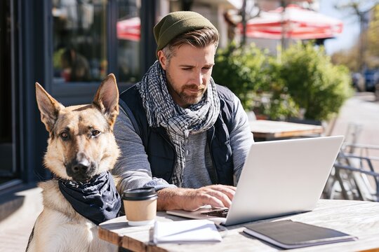 Modern pet ownership lifestyle of man with dog while working at outdoor cafe on sunny day