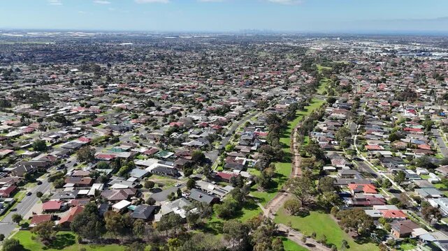 Aerial panorama of grassy drainage reserve corridor and linear parkland running through residential housing estates in Hoppers Crossing, Victoria, Australia, with distant Melbourne skyline