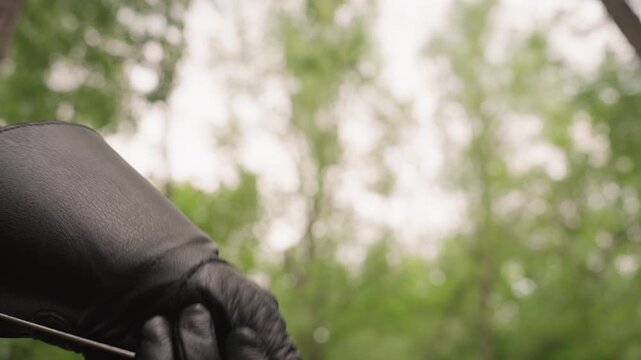 Close up of gloved hand holding and manipulating old fashioned sword with visible metal blade wooden handle. background is consistently blurred green foliage. Soft natural light illuminates