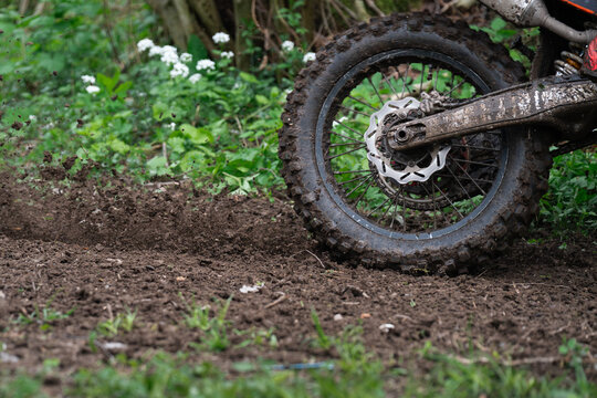 Frozen motion close-up capturing a motocross or enduro motorcycle rear knobby tire accelerating on a muddy off-road track. Flying soil spray and heavy debris concept representing extreme motorsport