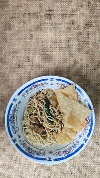 Delicious bowl of traditional Indonesian chicken noodles, locally known as Mie Ayam, topped with seasoned diced chicken, green vegetables, and served with crispy deep fried wonton crackers.
