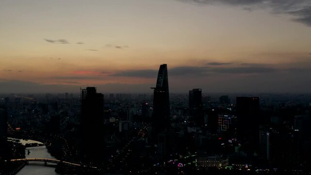 Aerial drone view of Ho Chi Minh City at sunset, featuring Bitexco Financial Tower, Ba Son Bridge, the Saigon River and the modern downtown skyline of Vietnam.