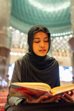 Young muslim woman reading holy quran in mosque