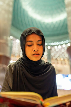 Muslim woman wearing hijab reading religious book