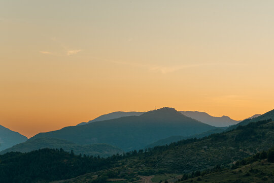 Beautiful silhouette of layered mountain ranges during a vibrant orange and yellow sunset in Verri, Albania.