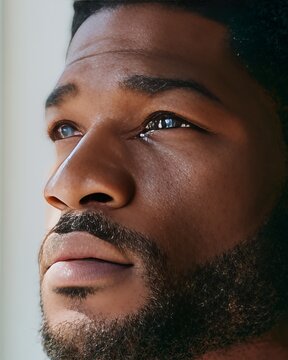 Close up of a Black man's face showing quiet subdued sadness, with a focus on his expressive eyes and facial features illuminated by soft natural light