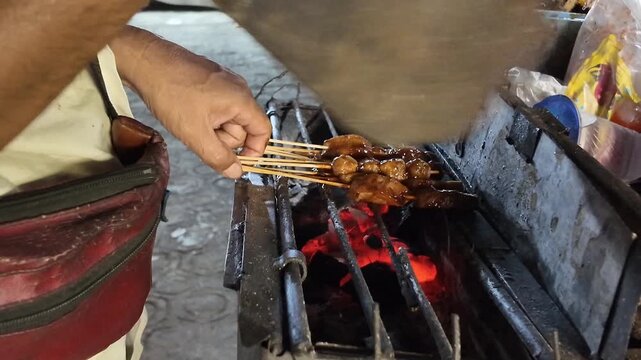 A lively grilling moment unfolds as skewers are brushed and turned over glowing charcoal, slowly developing a glossy, caramelized surface under the rising smoke.
