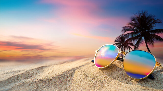 Sunglasses with sunset reflection on sandy beach with palm trees background banner