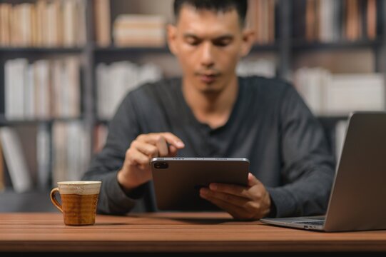 Young Man Using Tablet at Desk in Library with Books in Background