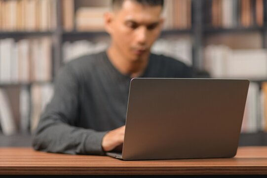 Young Man Using Laptop at Desk in Library with Bookshelf Background