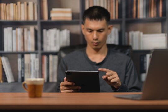 Young man using tablet device at desk in modern library or home office setting