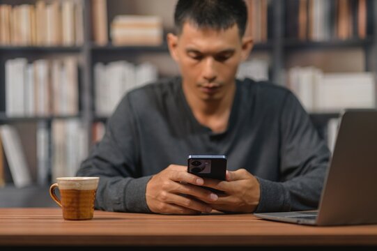 Man Sitting at Desk Using Smartphone in Office with Bookshelf Background