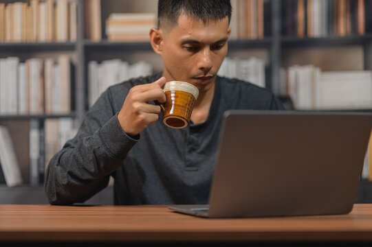Man Drinking Coffee While Working on Laptop in a Cozy Library Setting