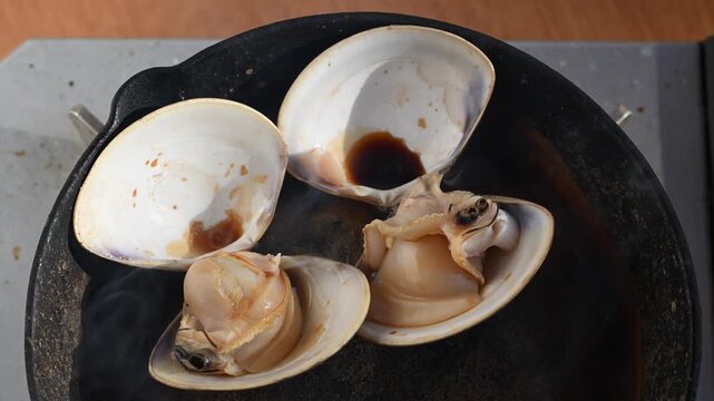 網焼きでぐつぐつと沸騰する醤油と湯気が立つ大粒のハマグリ