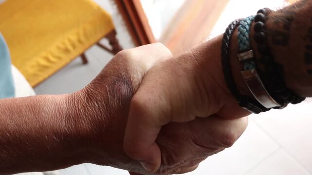 Close-up of a young tattooed man and an elderly man shaking hands, symbolizing an agreement between generations, trust, respect, and successful partnership in a bright indoor setting