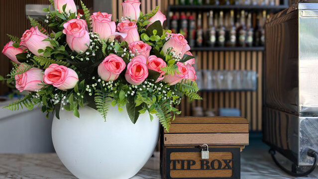 Wooden tip box beside decorative pink rose arrangement on a cafe counter, hospitality and customer service concept.