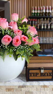 Wooden tip box beside decorative pink rose arrangement on a cafe counter, hospitality and customer service concept.