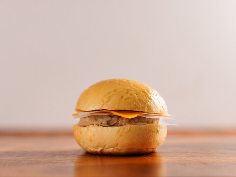 Classic hamburger layer with soft golden bun juicy meat beef or pork patty melted cheddar cheese present on rustic wooden table with warm natural lighting clean minimal background fresh tasty burger.