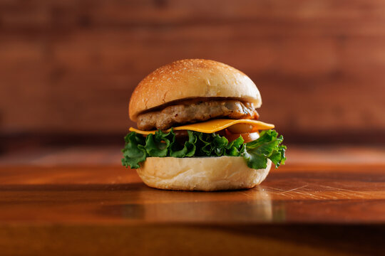 Delicious cheeseburger layer with golden bun juicy meat beef or pork patty melted cheddar cheese on wooden table background fresh ingredients green lettuce tomatoes tasty classic burger junk fast food
