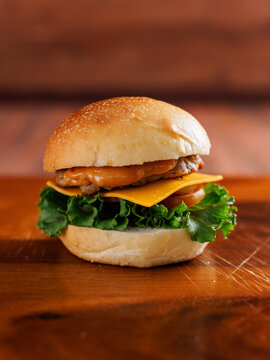 Delicious cheeseburger layer with golden bun juicy meat beef or pork patty melted cheddar cheese on wooden table background fresh ingredients green lettuce tomatoes tasty classic burger junk fast food
