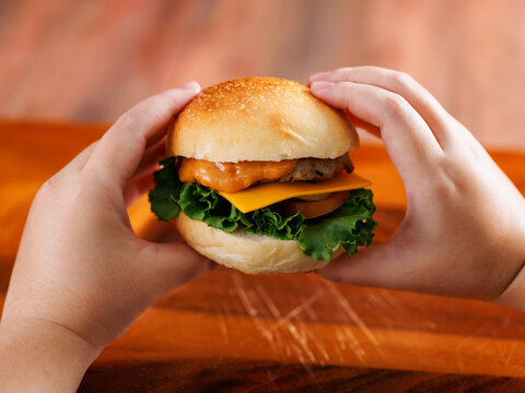 Two hand holding delicious cheeseburger layer with golden bun juicy meat beef or pork patty melted cheddar cheese on wooden background fresh ingredients lettuce tomatoes tasty classic burger junk food