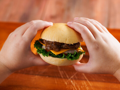 Two hand holding delicious cheeseburger layer with golden bun juicy meat beef or pork patty melted cheddar cheese on wooden background fresh ingredients lettuce tomatoes tasty classic burger junk food
