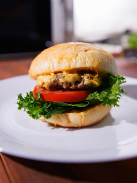 Delicious cheeseburger on plate layer with golden bun juicy meat beef or pork patty melted cheddar cheese on wooden table background fresh ingredients lettuce tomatoes tasty classic burger junk food