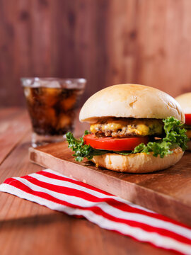 Delicious cheeseburger layer with golden bun juicy meat beef pork patty melted cheese on wooden table background sparkling soft drink with red striped cloth tasty classic burger fast food advertising.