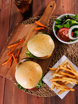 Fresh homemade cheeseburgers  juicy beef patties melted cheese lettuce tomato served on wooden board with crispy french fries creating delicious casual dining meal tasty classic fast food advertising.
