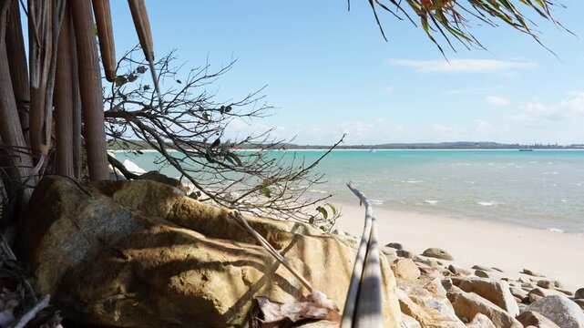 Pandanus palms and granite boulders above a white sand beach with yachts moored on turquoise Trial Bay, New South Wales, Australia
