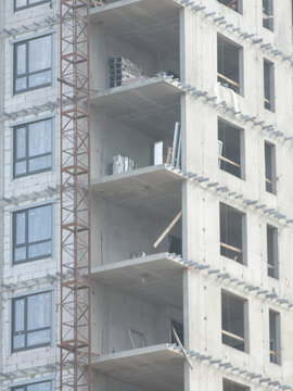 Unfinished multistory building with open balconies, installed windows and exposed facade sections during active construction. Urban development showing different stages of exterior completion and mode