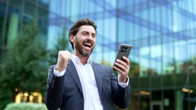 Excited mature businessman in a formal suit reacting to positive news on his smartphone in close up outside office building. Happy professional smiling with pleasant surprise while reading a message
