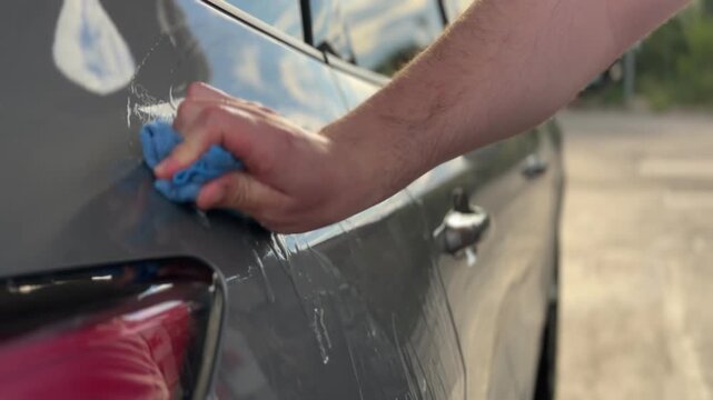 A person cleaning a car door with a microfiber cloth outdoors.