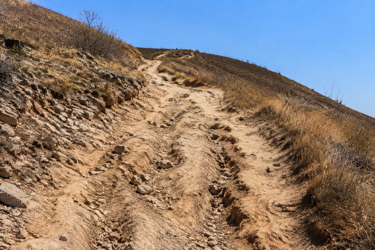 Steep unpaved trail on dry rocky hillside with ruts and exposed roots, arduous hiking path concept