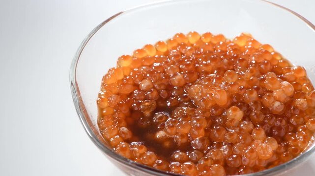 Fresh salmon roe in soy sauce marinade showcased in a glass bowl with glossy texture