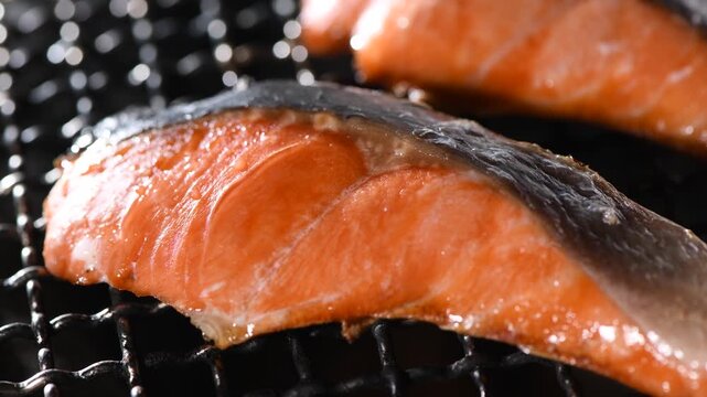 Grilled salmon fillet cooking on a charcoal grill grate, camera zooms in and pans across the seared surface