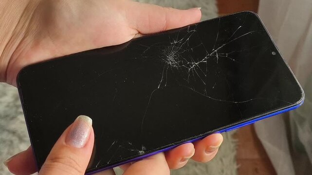Woman attempting to turn on a smartphone with a shattered touchscreen, broken display and damaged device, electronics repair and battery replacement concept.
