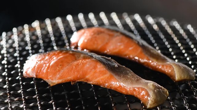 Fresh salmon fillets grilled over charcoal on traditional Japanese shichirin grate with golden sizzle